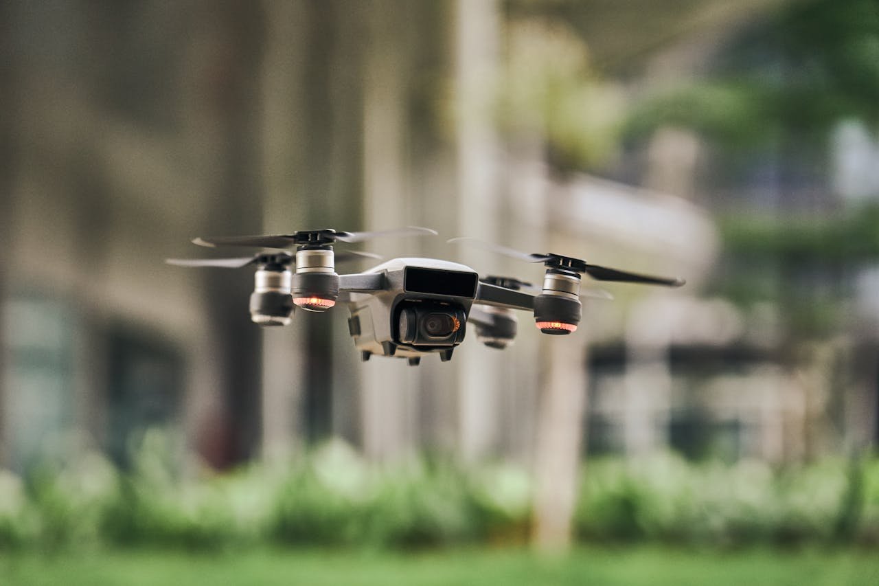 Close-up of a modern quadcopter drone hovering outdoors with blurred greenery background.